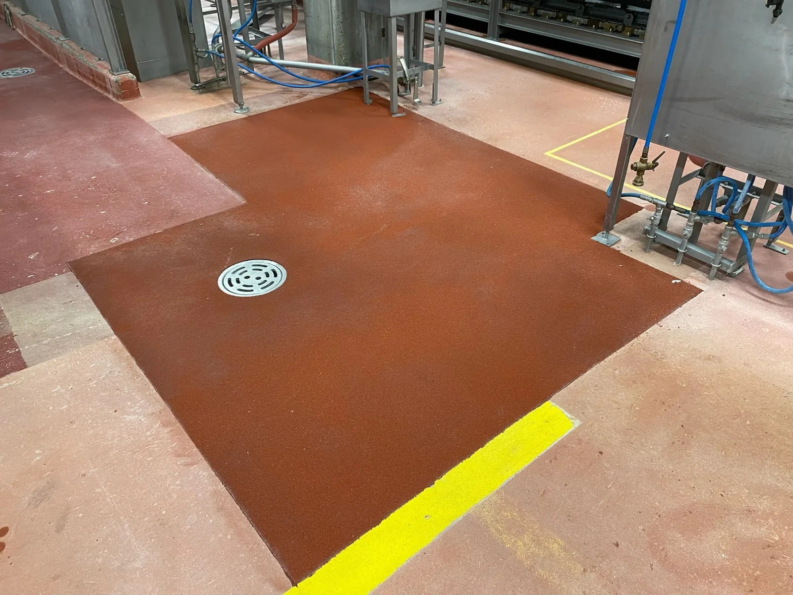 Brown industrial floor coating with yellow safety lines around stainless processing equipment