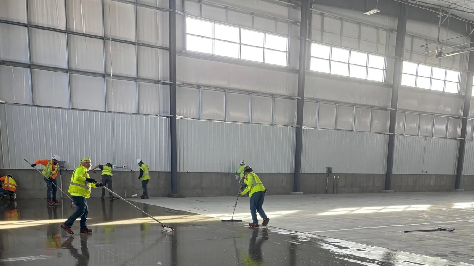 Crew spreading a dark resin floor coating across a large aircraft hangar